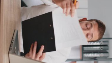 İş adamı CEO 'su iş sözleşmesi okuyor, proje planlıyor, özgeçmişi analiz ediyor, iyi kağıt işlerinden memnun. Ofisteki adam kameraya bakıyor, konuşuyor, online sohbet görüşmesi yapıyor. Dikey