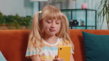 Child kid girl use smartphone, playing game, loses becoming surprised sudden lottery results, bad news, fortune loss, fail education study test. Female teen toddler at home in living room sits on sofa