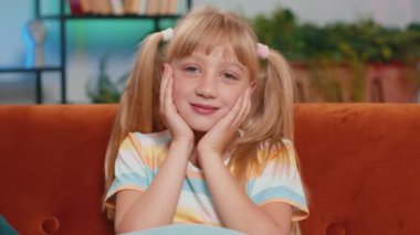 7 yaşındaki mutlu, beyaz, liseli bir kızın yakın plan portresi. Evdeki oyun odasındaki kanepede oturan sevimli sarışın çocuk kameraya bakıyor. At kuyruğu saç stili
