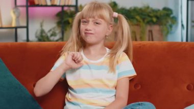 Dislike. Upset girl showing thumbs down sign gesture, expressing discontent, disapproval, dissatisfied bad work at modern home apartment indoors. Displeased teen child, kid in living room on sofa