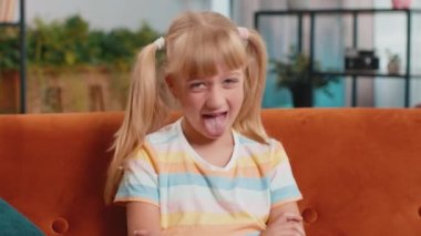 Kafkasyalı neşeli liseli kız şakacı aptal yüz ifadeleri takınıyor, suratını buruşturuyor, oynaşıyor, dil gösteriyor. Genç, heyecanlı, sarışın çocuk. Oturduğu evde, koltukta oturuyor.