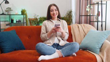 Kanepede oturan genç bir kadının portresi evde gülümseyen bir cep telefonu kullanıyor. Akıllı telefon sosyal medya uygulamaları üzerinden rahatlama filmi izlerken mesajları paylaşan kız