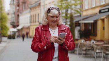 Gezici navigatör uygulamasında haritada bir yol bulmak için akıllı telefon kullanarak mesajlar yazan son sınıf kadınının portresi. Şehir sokaklarında yürüyen yaşlı bir büyükanne. Kasaba yaşam tarzları