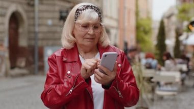 Zeki telefonlar kullanarak internete mesajlar yazarak, işi bitirerek, kameraya bakarak yorgun ve bitkin bir şekilde gülümseyen yaşlı kadın. Şehir caddesinde yürüyen olgun bir büyükanne. Şehir dışında.