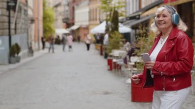 Kablosuz kulaklıklar takmış, açık havada dans ederek en sevilen disko rock 'n roll müziğini dinleyen mutlu, gevşemiş son sınıf kadını. Büyükannem şehir caddesinde yürüyor.