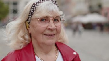 Mutlu son sınıf kadınının yakın plan portresi güler yüzlü, güler yüzlü kameraya bakan mutlu yüz hayal kuran, dinlenen, rahatlayan, dışarıda iyi haberler veren. Şehir sokağındaki büyükanne.