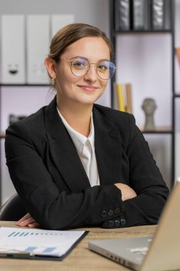 Ofis masasında kameraya bakan mutlu beyaz iş kadınının portresi. Resmi beyaz gömlekli bir kadın. Bilgisayarla çalışan uzaktan kumandalı güzel bir genç kız. Dikey
