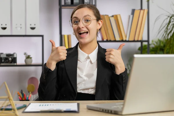 快乐的白人女商人在笔记本电脑上工作时 赞许地看着展示大拇指的相机 就像在办公室里签积极正面的东西 积极的反馈 自由职业者女孩 — 图库照片