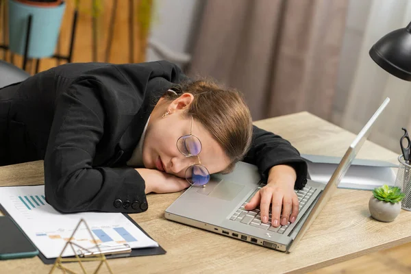 疲惫困倦的白种人女商人 戴着眼镜工作在笔记本电脑上 手牵着手睡着在办公室里 疲惫不堪的自由职业者是个工作狂 无工作就业职业 — 图库照片