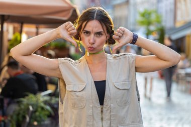 Hoşlanmamak. Üzgün, güzel genç bir kadın, işaret dilini gösteriyor, hoşnutsuzluğunu, memnuniyetsizliğini, kötü işini, hatasını ifade ediyor. Memnuniyetsiz kız şehir merkezinde yaz caddesinde yürüyor.