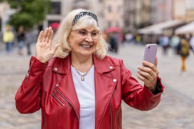 Üst düzey kadın blogcu akıllı telefondan selfie çekiyor, abonelerle online video görüşmesi yapıyor, sosyal medya vlog 'u için hikayeler kaydediyor. Şehir caddesinde yürüyen yaşlı büyükanne