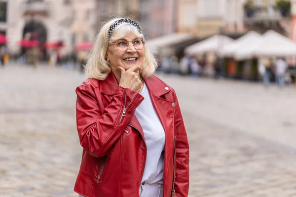 stock image Thoughtful pensive puzzled senior woman with pensive expression, pondering a solution, doubting question, thinking inspiration dreaming outdoors. Mature grandmother in city street. Town lifestyles