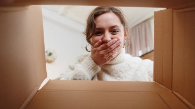 Inside view from box. Young happy woman unpacking delivery parcel at home. Smiling satisfied girl shopper, online shop customer opening cardboard receiving purchase gift by fast postal shipping order