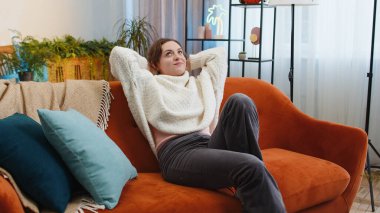 Yorgun genç bir kadının portresi evdeki kanepede dinlenmenin keyfini çıkarıyor. Mutlu güzel kız kanepede uzanmış dinleniyor yorucu bir günün ardından kestiriyor gözlerini kapatıyor, ellerini başının arkasına koyuyor, stresten kurtuluyor, dinleniyor.