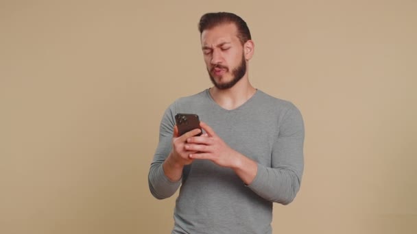 レバノン人は 携帯電話の携帯電話の入力のブラウジングを使用すると 突然宝くじの結果 失敗に驚いて失う ハンサムな中東の男はベージュのスタジオの背景に隔離され — ストック動画