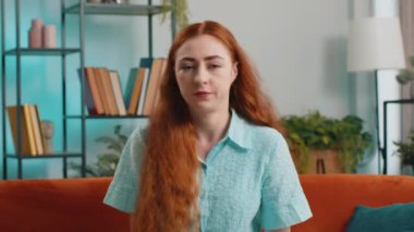 Memnun olmayan kızıl saçlı bir kadın nahoş berbat bir fikre tepki veriyor, kötü kaliteden memnun değil, el sallıyor, başını sallıyor. Evdeki kanepede oturan kız.