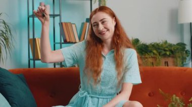 Kızıl saçlı emlakçı kadın yeni ev dairesinin anahtarlarını gösteriyor, ev satın alıyor ya da kiralıyor, ev kredisi veriyor. Odadaki kız kanepede oturuyor.