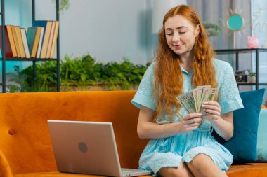 Planlama bütçesi. Zengin, mutlu, kızıl saçlı, nakit sayan ev faturalarını hesaplayan dizüstü bilgisayar kullanan bir kadın. Neşeli kız gelir sağlar, planlı tatil için para biriktirir, hediyeler