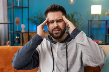 Baş ağrısı problemini tedavi etmek için tapınakları ovuşturan hoşnutsuz bir adam, tansiyon ve migrenden muzdarip, evde acı içinde kıvranan yüksek tansiyon. Kanepede oturan beyaz adam. Yaşam Tarzları