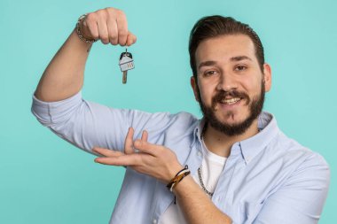 Genç Lübnanlı emlakçı el kaldırıyor. Yeni ev dairesinin anahtarlarını gösteriyor. Mülk alıyor ya da kiralıyor. Sakallı Arap adam mavi stüdyo arka planında izole edilmiş.