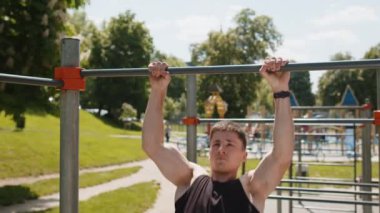 Athletic caucasian man in sportswear doing pull ups exercises on horizontal bar. Young guy pumping up back muscles on summer playground. Sports, health, fitness routine, workout. Strength, motivation