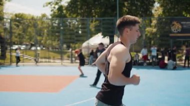 Spor giyimli beyaz bir adam basketbol sahasında koşuyor. Genç sporcu yazın şehir parkında koşmaktan zevk alıyor. Spor sağlık programı, antrenman. Motivasyon. Açık havada.