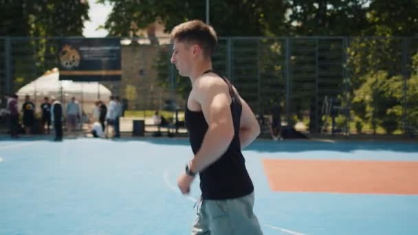 バスケットボールコートでスポーツウェアジョギングをしている陸上競技の白人男性 都会の夏の遊び場でランニングを楽しむ若いスポーツマン スポーツ健康フィットネスルーチン ワークアウト やる気だ — ストック動画
