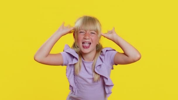 陽気で面白いいじめっ子の若いかわいい女の子は カメラで顔を作る舌を示す 周りを欺く 愚かな顔で からかって からかっている 黄色の背景に金髪の子供の子供の前に 小さな子供たち — ストック動画