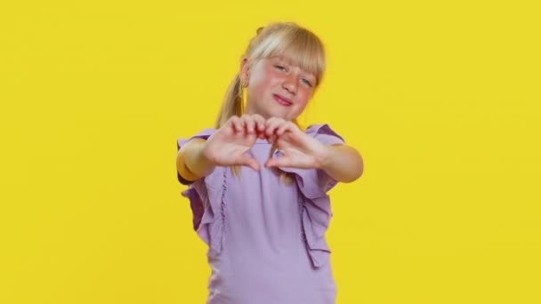我爱你I Love You 笑着年轻可爱的金发女学生做的心形表示爱意 表示好感和同情 在工作室黄色背景下被隔离的少女时代快乐的小女孩 — 图库视频影像