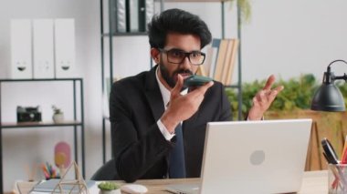 Sakallı Hintli iş adamı ofis masasında dizüstü bilgisayarla cep telefonu hoparlörü ile konuşuyor. Menajer serbest çalışan Hintli adam haberci sohbet uygulamaları kullanarak akıllı telefon tutuyor. İstihdam, meslek