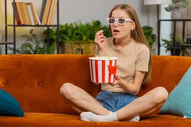 Kanepede oturup patlamış mısır yiyen ve ilginç TV dizileri, spor oyunları, filmler, evdeki sosyal medya içerikleri izleyen heyecanlı genç bir kadın. Üç boyutlu gözlüklü kız ev eğlencesi yapıyor.