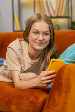 Kanepede uzanan kadın evde gülümseyen cep telefonu kullanıyor. Akıllı telefon sosyal medya uygulamaları üzerinden rahatlama filmi izlerken mesajlarını paylaşan genç bir kız. Dikey