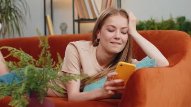 Kanepede uzanan kadın portresi evde gülümseyen cep telefonu kullanıyor. Akıllı telefon sosyal medya uygulamaları üzerinden rahatlama filmi izlerken mesajları paylaşan genç kız