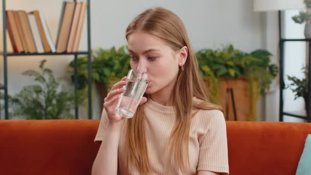 天然のアクアグラスを持っている喉の渇き若い女性は 自宅のリビングルームに脱水症状を防ぐために まだ水を飲んでお尻を作る 良い生活習慣 健康的な痩身 減量の概念を持つ女の子 — ストック動画