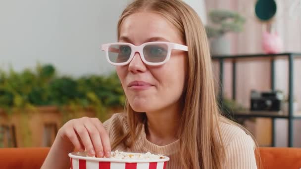 兴奋的年轻女子坐在沙发上吃爆米花 在家里看有趣的电视连续剧 体育比赛 在线社交媒体电影内容 戴3D眼镜的女孩享受家庭娱乐 — 图库视频影像