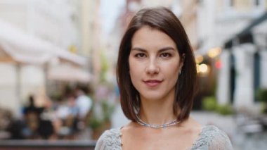 Mutlu güzel bir genç kadının portresi. Dostça gülümseyen, kameraya bakan mutlu yüz ifadesi. Hayal kuran, dinlenen, rahatlayan, dışarıda iyi haberler veren. Kentsel şehir Avrupa sokak geçmişinde bir kız