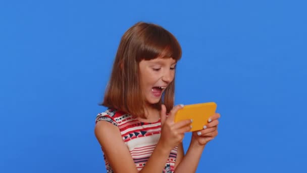 忧心忡忡的年轻女生兴致勃勃地在智能手机上玩赛车或射击游戏 使用带有蓝色背景驱动器模拟器的智能手机小应用程序的青少年白人儿童 — 图库视频影像