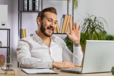 Ofis masasında dizüstü bilgisayarda çalışan bir iş adamı çalışanla online iletişim videosu konuşması yapıyor. Bilgisayar kameralarına bakan yönetici-patron destek servisleri