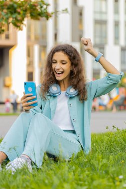 Ergenlik çağındaki çocuk cep telefonu kullanıyor. Kutlama yapıyor. İyi haberler alıyor, piyango ikramiyesi kazanıyor, internetten dağıtıyor. Şehir merkezindeki şehir parkında çimlerde oturan mutlu kız. Dikey