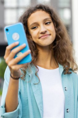 Gülümseyen ergen çocuk akıllı telefon kullanıyor mesajlar yazıyor internette geziniyor, işi bitiriyor, dışarıdaki kameralara bakıyor. Şehir caddesinde yürüyen bir kız turist. Kasaba yaşam tarzları. Dikey çekim