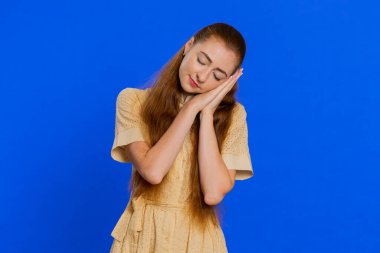 Yorgun, genç bir kadın avuçlarında uzanarak uyuyor, esniyor, gündüzleri uyukluyor, dinleniyor, rahat bir uyku zamanı. Kızıl saçlı kız mavi stüdyoda kapalı alanda izole edilmiş.