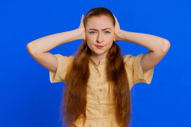 Duymak ve dinlemek istemiyorum. Sinirli, sinirli, kulaklarını tıkayan, tavsiye almayan, gürültülü sesleri görmezden gelen bir kadın. Kızıl saçlı yetişkin kız mavi arka planda tek başına.