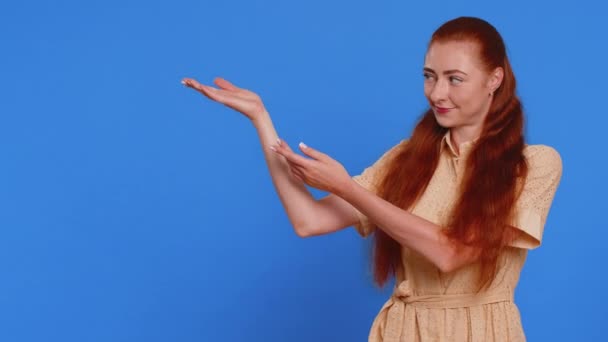 親指を示し 空の場所を指す若い女性 商業テキストのための広告区域 商品の昇進の広告のためのコピーのスペース 青いスタジオで孤立した赤毛の少女 ライフスタイル — ストック動画