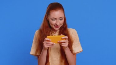 Endişeli komik bağımlı kadın cep telefonuyla yarış oyunları oynuyor. Mavi stüdyo arka planında izole edilmiş sürücü simülatörlü akıllı telefon uygulaması kullanan mutlu genç kız.