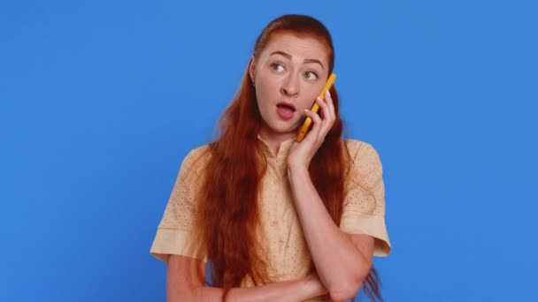 疲れた眠っている若い美しい女性は オンライン会話をする友人と携帯電話で話しています 興味深い赤毛の大人の少女は青い背景で隔離されたスマートフォンで迷惑な退屈な話をする — ストック動画