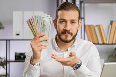 Ortadoğulu genç işadamı nakit para gösteren bir işadamı size iyi bir işten tatmin olmuş maaşlar veriyor. Başarı, servet, yatırım. İş yerindeki serbest çalışan adam kameraya bakıyor.