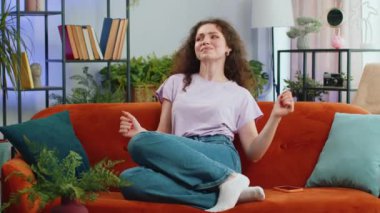 Modayı takip eden neşeli genç bir kadının portresi dans etmek ve ritme ayak uydurmak, ellerini ovuşturmak, dublaj birincisi jestini koltukta oturarak kutlamak. Oturma odasındaki kız.