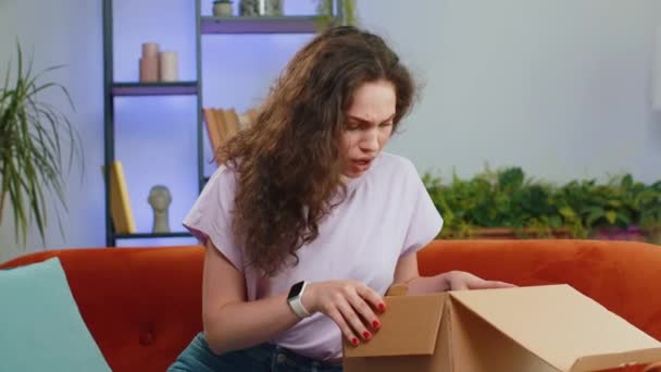 愤怒而又不满意的购物者打开包装的年轻女人对从网上商店的错误送货 家里劣质购物感到心烦意乱 在屋里沙发上的一个成年姑娘 — 图库视频影像