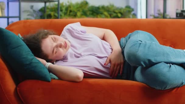 生病的女人肚子痛 在家里的沙发上躺着阵阵抽筋 抱着肚子 感觉腹部或月经期疼痛的女孩 腹部疼痛 消化不良 — 图库视频影像