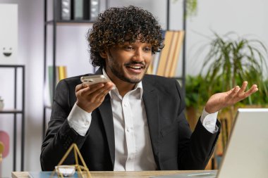 Sakallı Hintli iş adamı ofis masasında dizüstü bilgisayarla cep telefonu hoparlörü ile konuşuyor. Menajer serbest çalışan Hintli adam haberci sohbet uygulamaları kullanarak akıllı telefon tutuyor. İstihdam, meslek